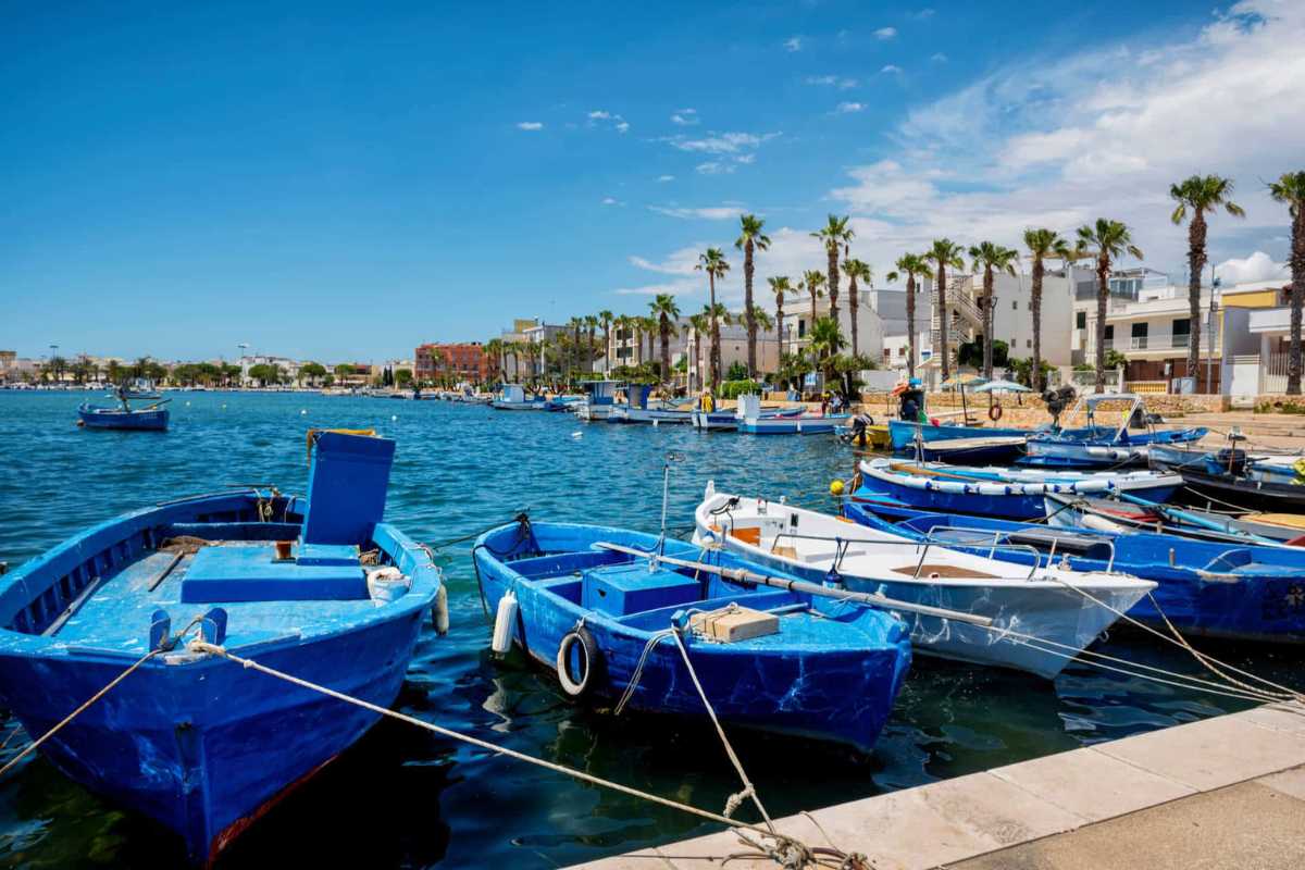 Scorcio panoramico della spiaggia di Porto Cesareo con mare turchese, barche dei pescatori e centro storico sullo sfondo